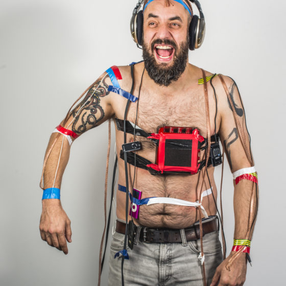 Jonny Cotsen laughing with sound recording equipment and headphones taped to his head and body.